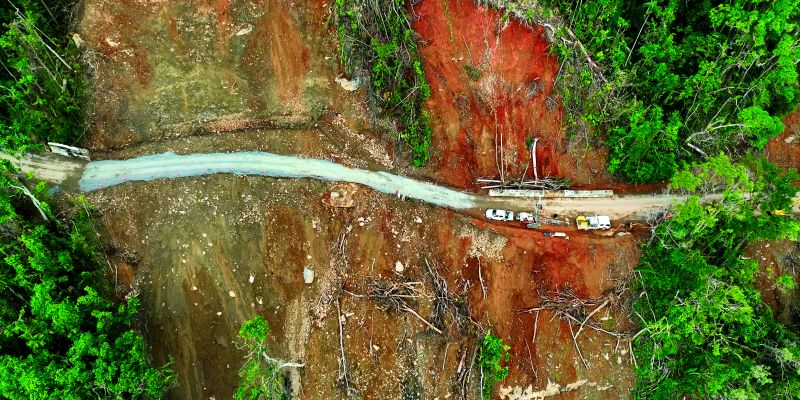 Aerial view of road repairs post a landslide on a steep hill in a rainforest.
