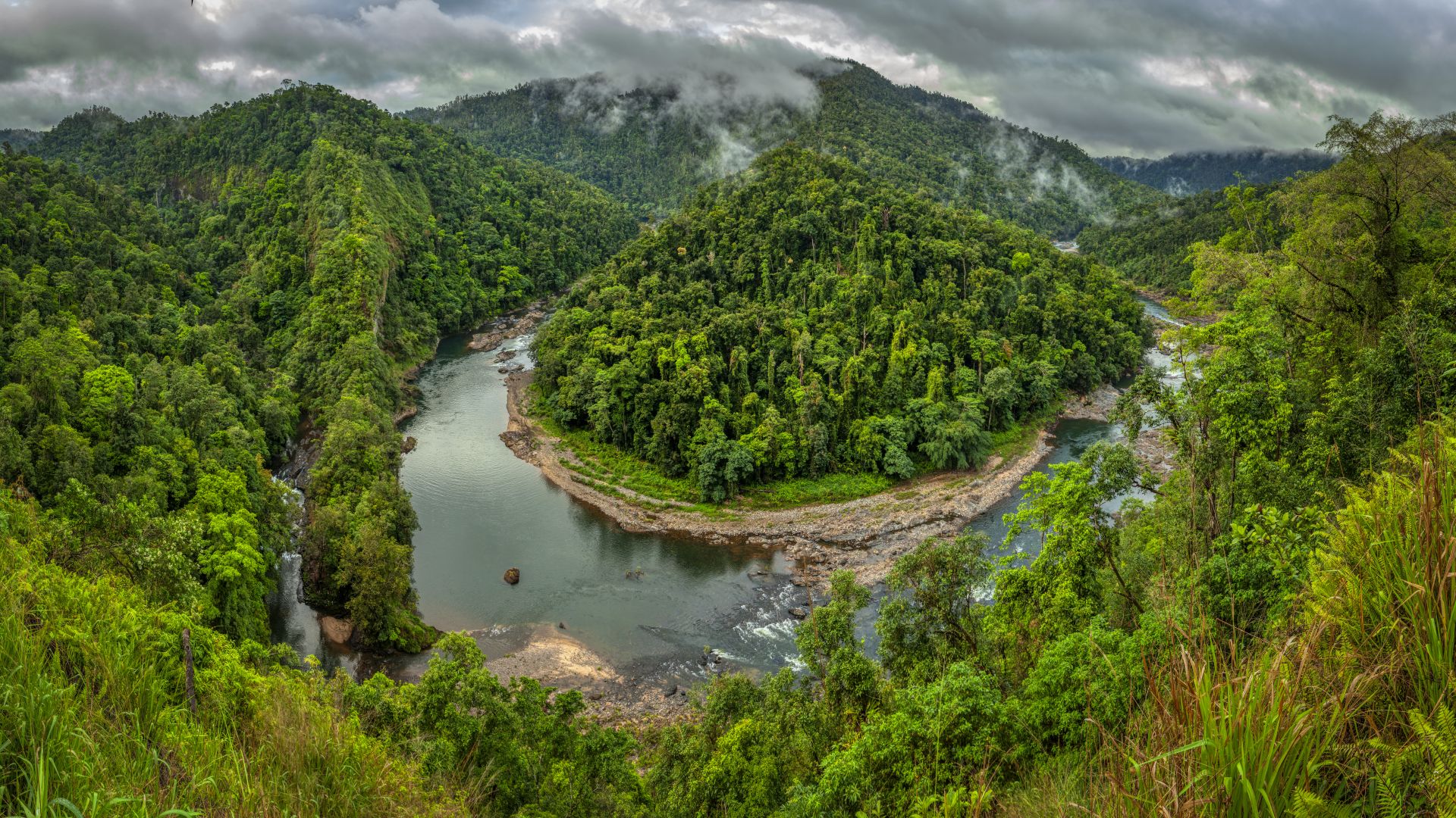 Aerial view of winding river through hilly rainforest.