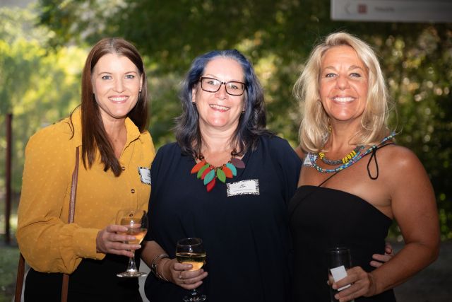 Three women with drinks at a networking event.