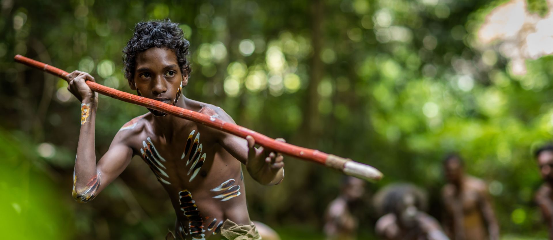 Indigenous youth with spear and body paint in a rainforest